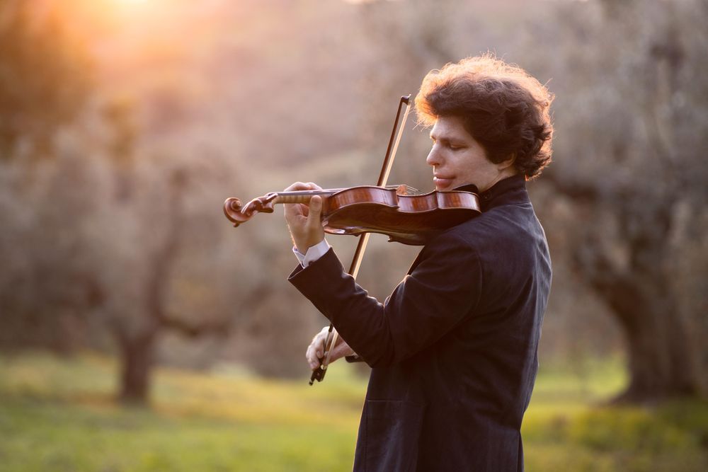 Augustin Hadelich mit Violine vor Bäumen